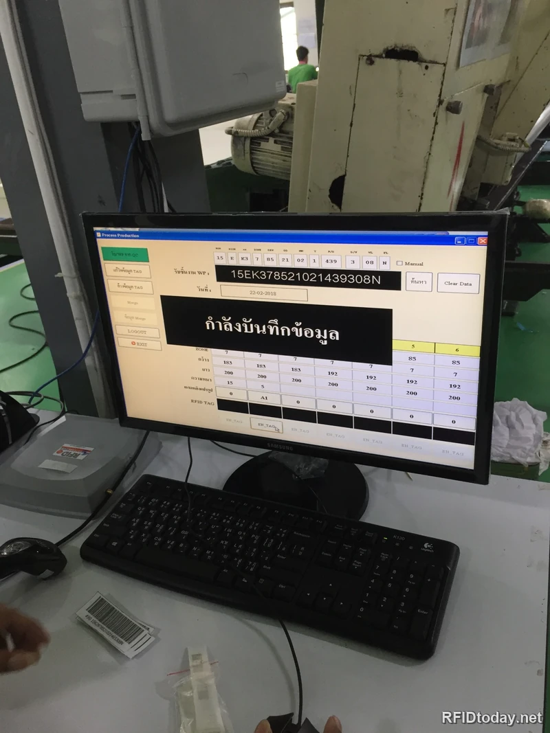สถานีออกแท็กที่หน้างาน มีจอแสดงโปรแกรม Process Production ที่กำลังบันทึกข้อมูล พร้อมคีย์บอร์ด เครื่องยิงบาร์โค้ด เครื่องอ่านเขียน Tag และป้ายบาร์โค้ดที่พิมพ์ออกมาวางอยู่บนโต๊ะ