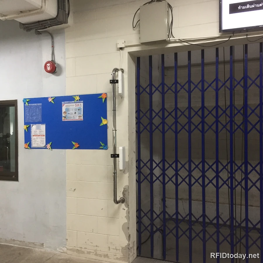 ปากลิฟท์ขนสินค้าที่ปิดด้วยประตูเหล็กยืด มีเสาอากาศ RFID สีขาวยึดอยู่กับผนังทั้งสองข้างของช่องประตู พร้อมตู้ควบคุมด้านบนและจอแสดงผลที่มุมขวาบน